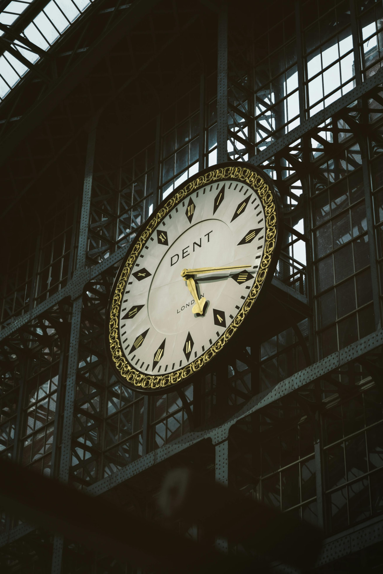 A Dent of London station clock beneath Victorian ironwork